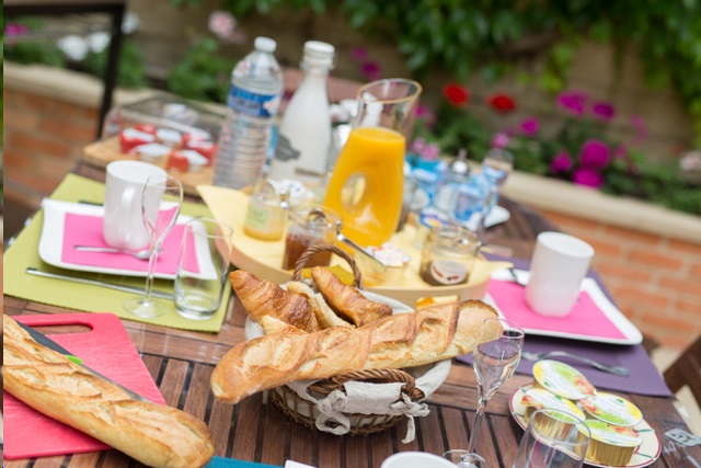 On voit la table du petit-déjeuner dressée sur la terrasse avec les produits frais à déguster en profitant du soleil et du jardin.