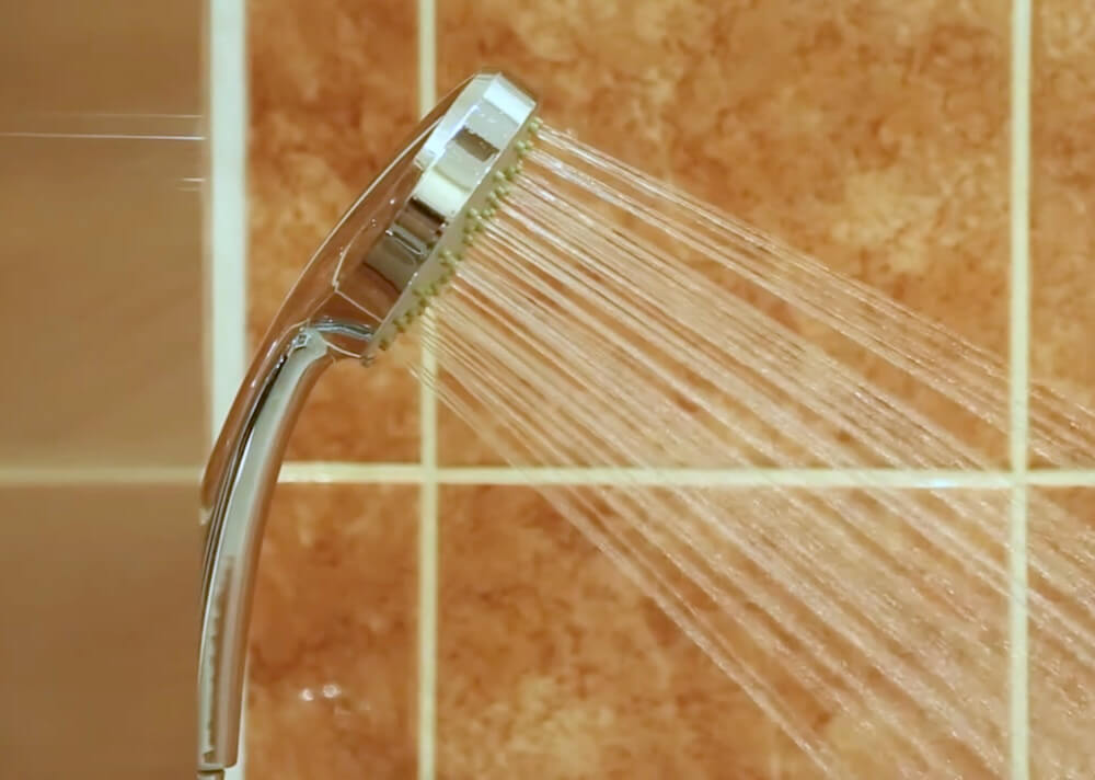 On voit un pommeau de douche avec l’eau qui coule dans la douche d’une chambre de Linterfaces