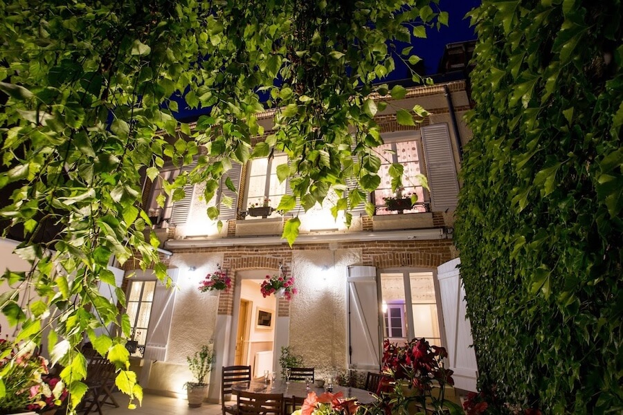 On aperçoit la façade et la terrasse de Linterfaces chambres d’hôtes de nuit éclairées par des lumières dans un cadre verdoyant