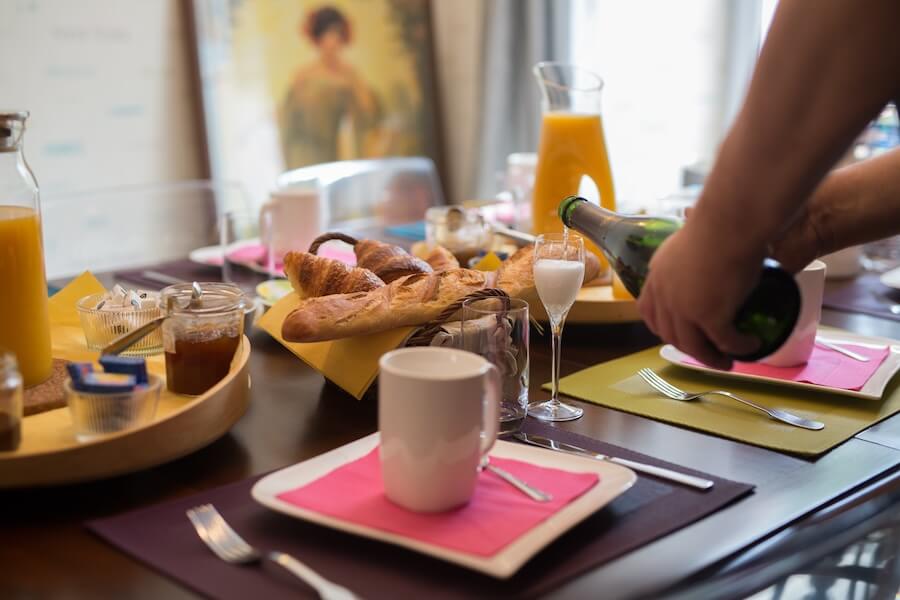 Une vue resserrée de la table du petit-déjeuner avec les baguettes, viennoiseries, le jus d’orange. Didier sert la coupe de Champagne offerte aux adultes.